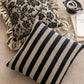 Two decorative pillows, one with black floral pattern and ruffled edge, the other with black and beige stripes, on a textured surface.