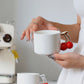 Person holding a white mug with cherry handle in a kitchen setting
