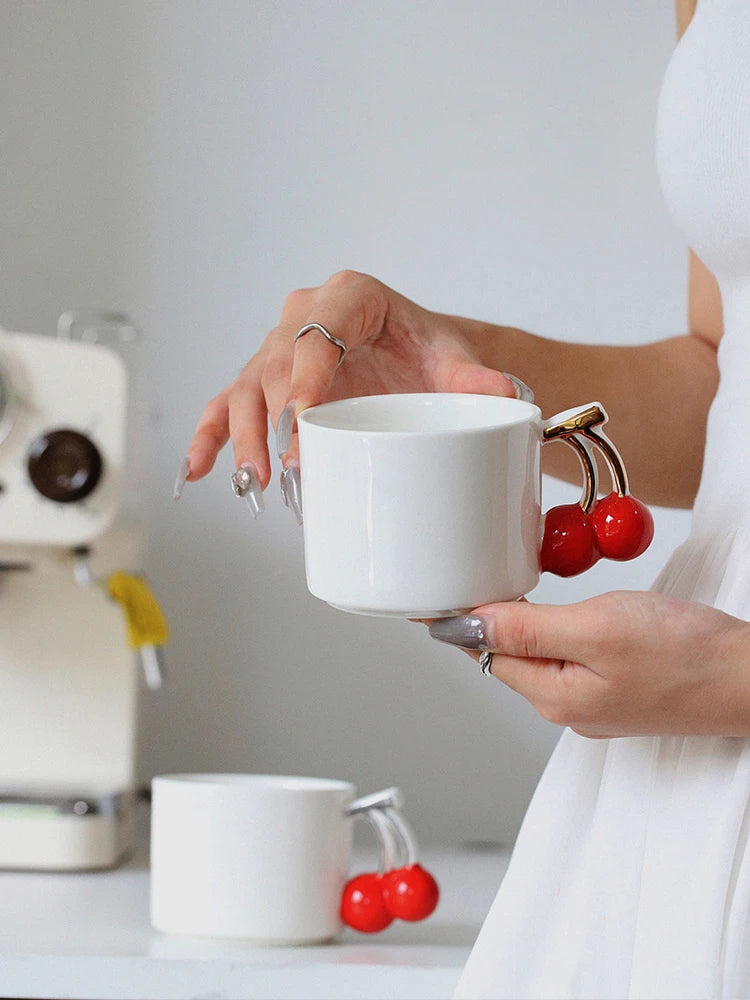 Person holding a white mug with cherry handle in a kitchen setting