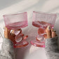 Pink glass goblets held by a person on a light surface