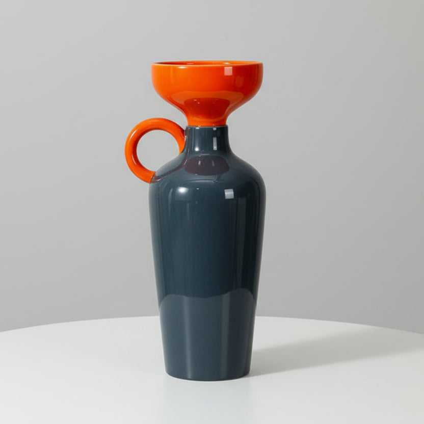 Vase with orange top and black body on a white surface against a textured wall.