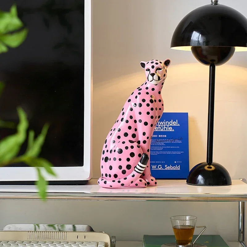 Pink and black spotted ceramic cheetah figurine on a shelf with a lamp and book in the background.