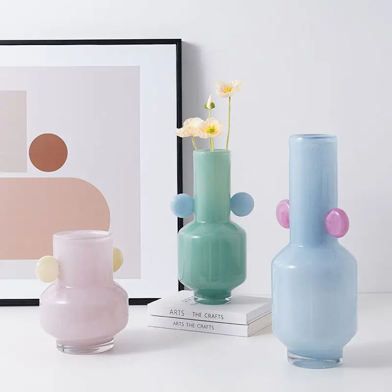 Three colorful vases on a white surface with a framed abstract art piece in the background.