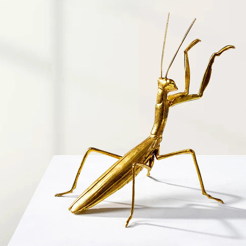Gold praying mantis sculpture on a white surface with a white background