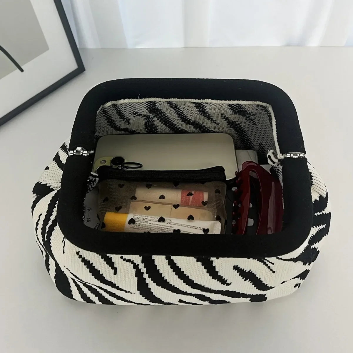 Zebra-patterned makeup bag with personal items on a white surface