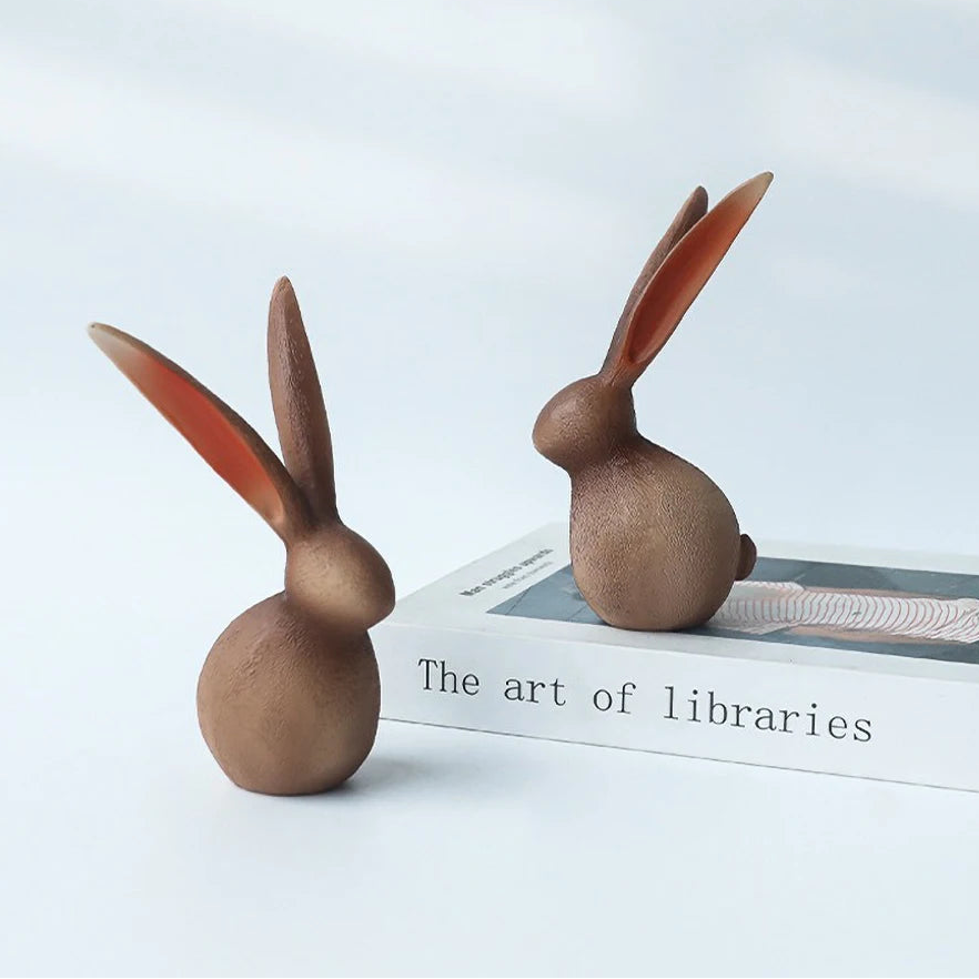 Two wooden rabbit figurines on a book titled 'The art of libraries' with a light gray background.