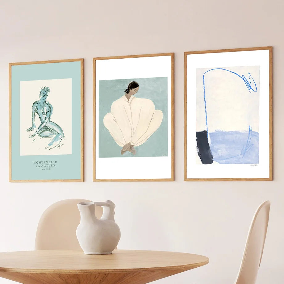Three framed artworks on a wall above a wooden table with a vase.