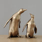 Two bronze penguin statues on a wooden surface with a gray background