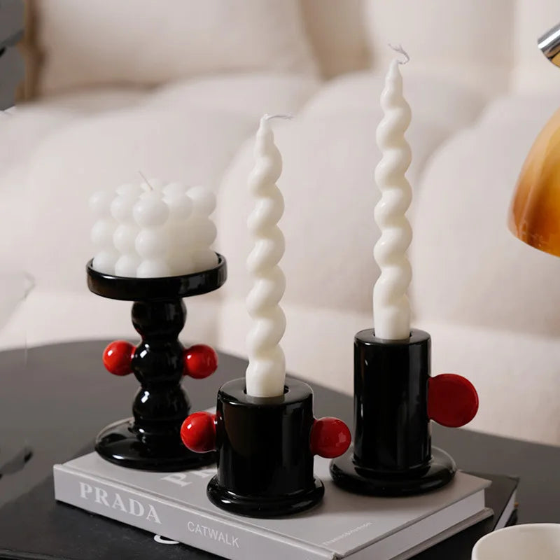 Three spiral candles on black holders with red accents on a Prada book