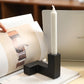 Black candle holder with a white candle on a magazine