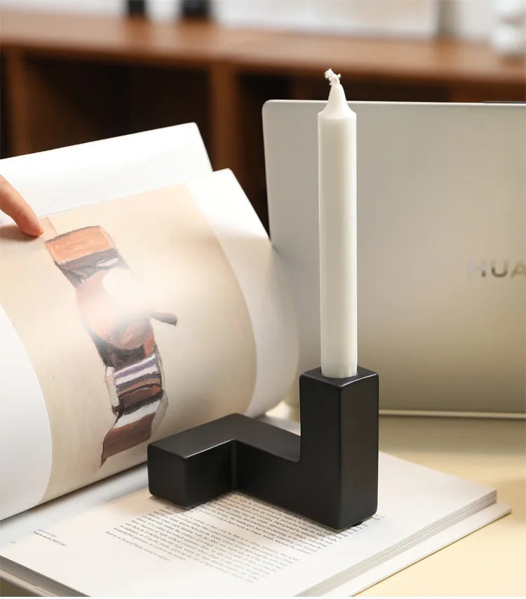 Black candle holder with a white candle on a magazine