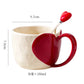 Ceramic mug with red heart-shaped handle and spoon on a white background