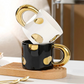 Two mugs, one black with gold polka dots and one white with gold accents, on a wooden tray.