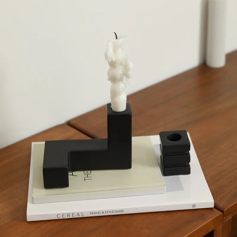 Black geometric candle holder with a white candle on top of a book