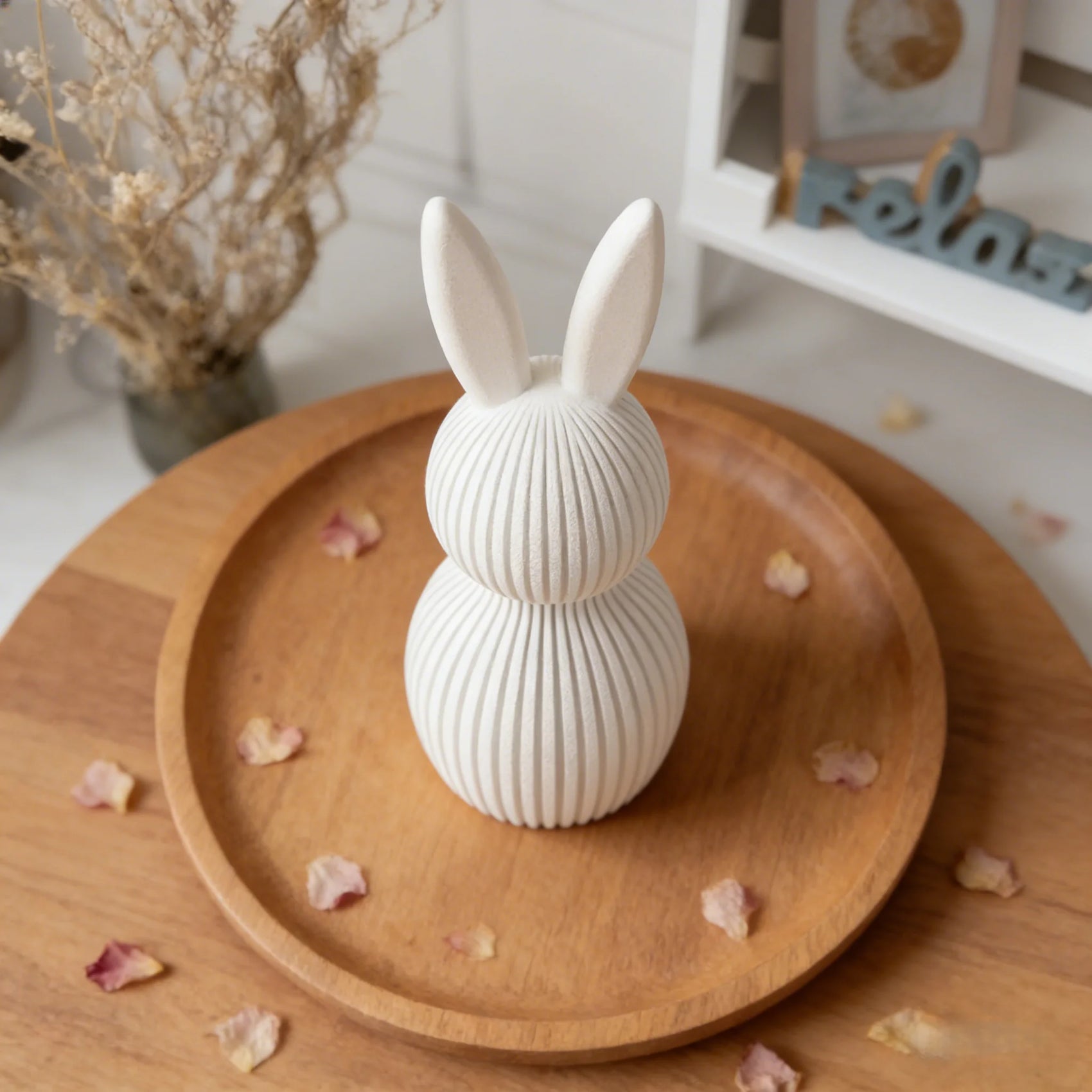 White rabbit-shaped decorative item on a wooden plate with dried flowers.