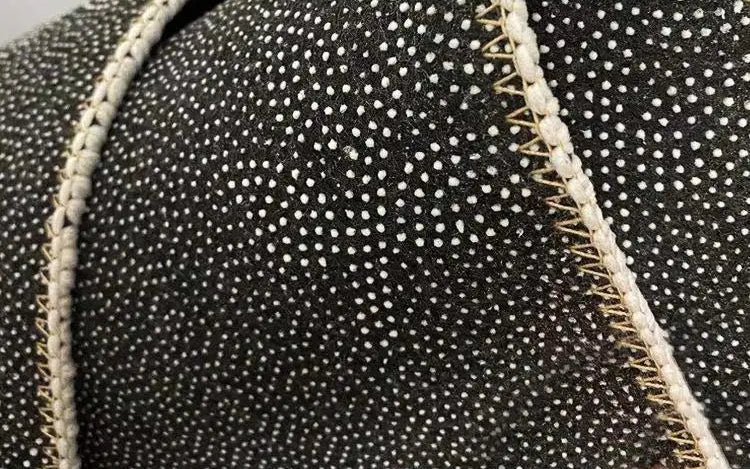Close-up of textured black fabric with white spots and beige stitching