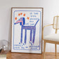 Framed artwork with a blue dog illustration and text on a wall in a room with a chair and decor items.