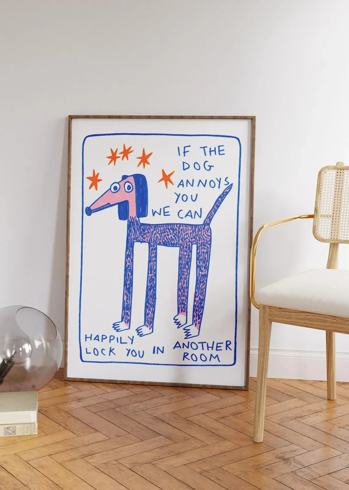 Framed artwork with a blue dog illustration and text on a wall in a room with a chair and decor items.