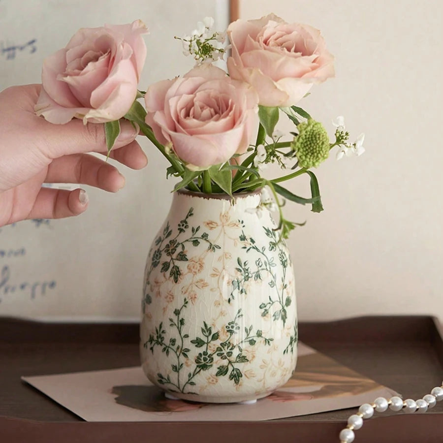 Decorative vase with floral pattern holding pink roses on a wooden surface.