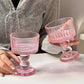 Two pink glass dessert dishes held by a person on a white surface.