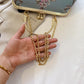 Gold chain necklace held by a hand with a beige bag and floral pattern in the background
