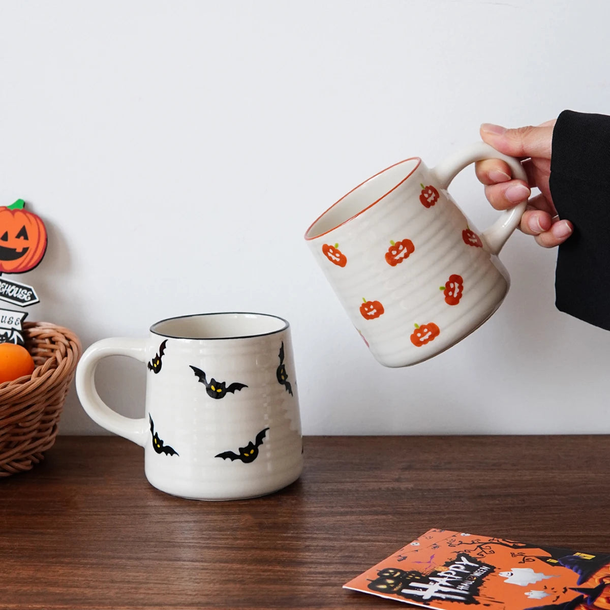 Two Halloween-themed mugs on a wooden surface with decorative items.