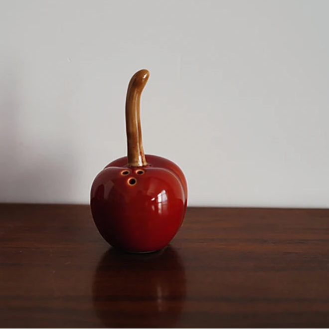 Red ceramic apple-shaped object with a brown stem on a wooden surface.