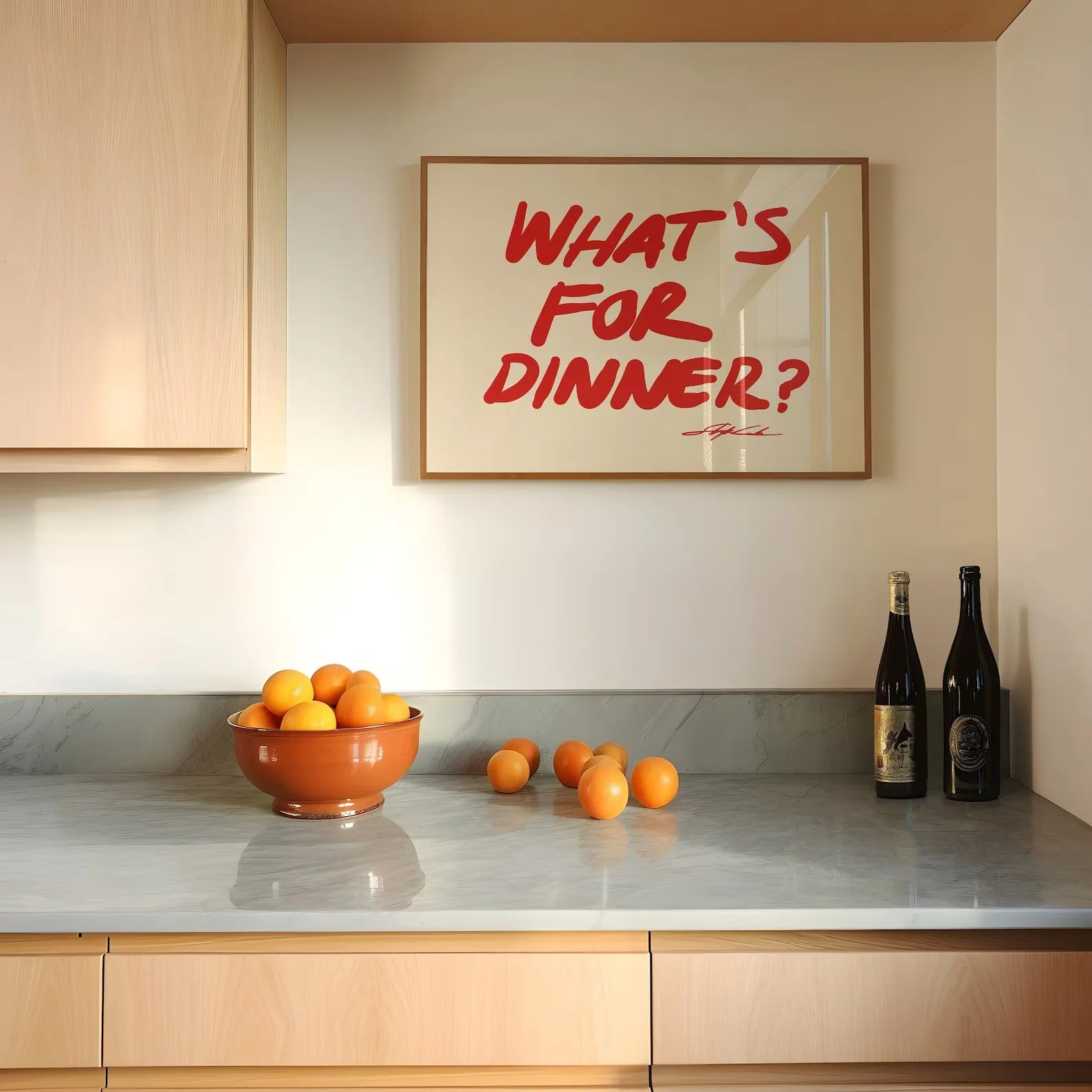 Modern kitchen with a bowl of oranges, a bottle of wine, and a framed question on the wall.