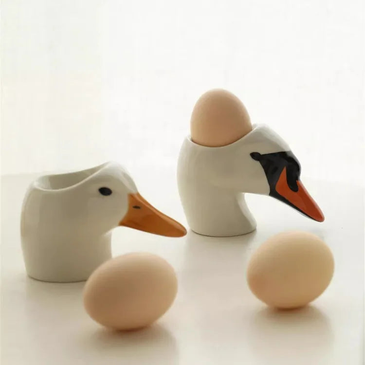 Ceramic duck and swan egg cups with eggs on a white background