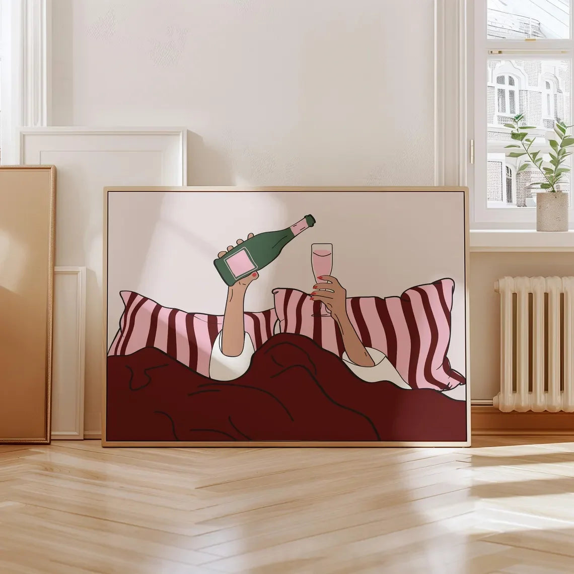 Framed artwork of a person lying on pillows with a bottle and glass, in a room with a window and radiator.