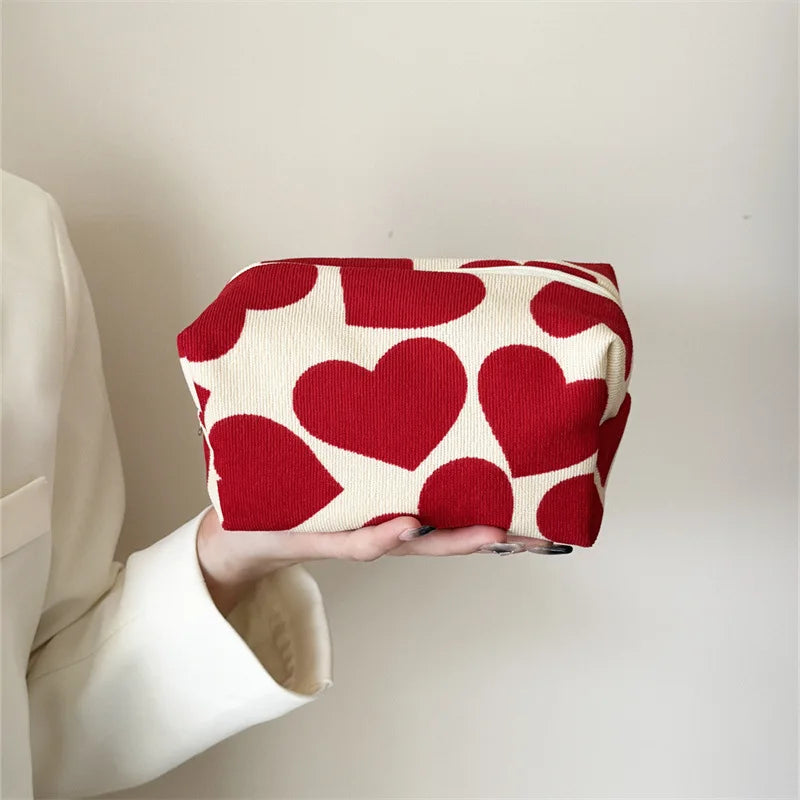 Person holding a red heart-patterned pouch against a neutral background