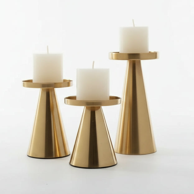 Three gold candle holders with white candles on a wooden surface.