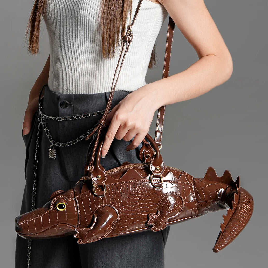 Person holding a brown alligator-shaped handbag with a plain background