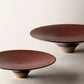 Two brown ceramic dinner plates with a high foot, one plate is in front of the other creating a layered look.