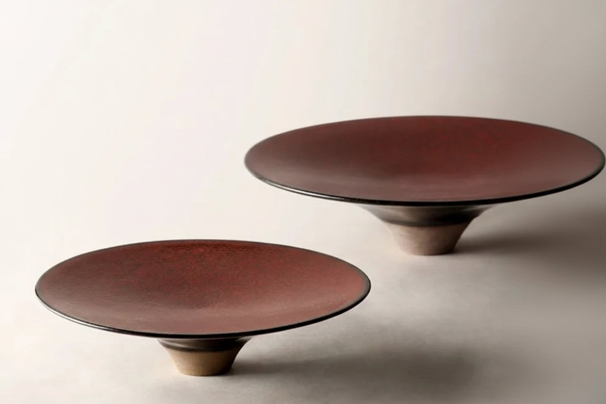 Two brown ceramic dinner plates with a high foot, one plate is in front of the other creating a layered look.