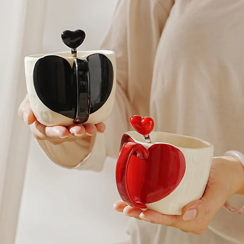 Two heart-shaped ceramic cups, one black and one red, held by hands against a neutral background.