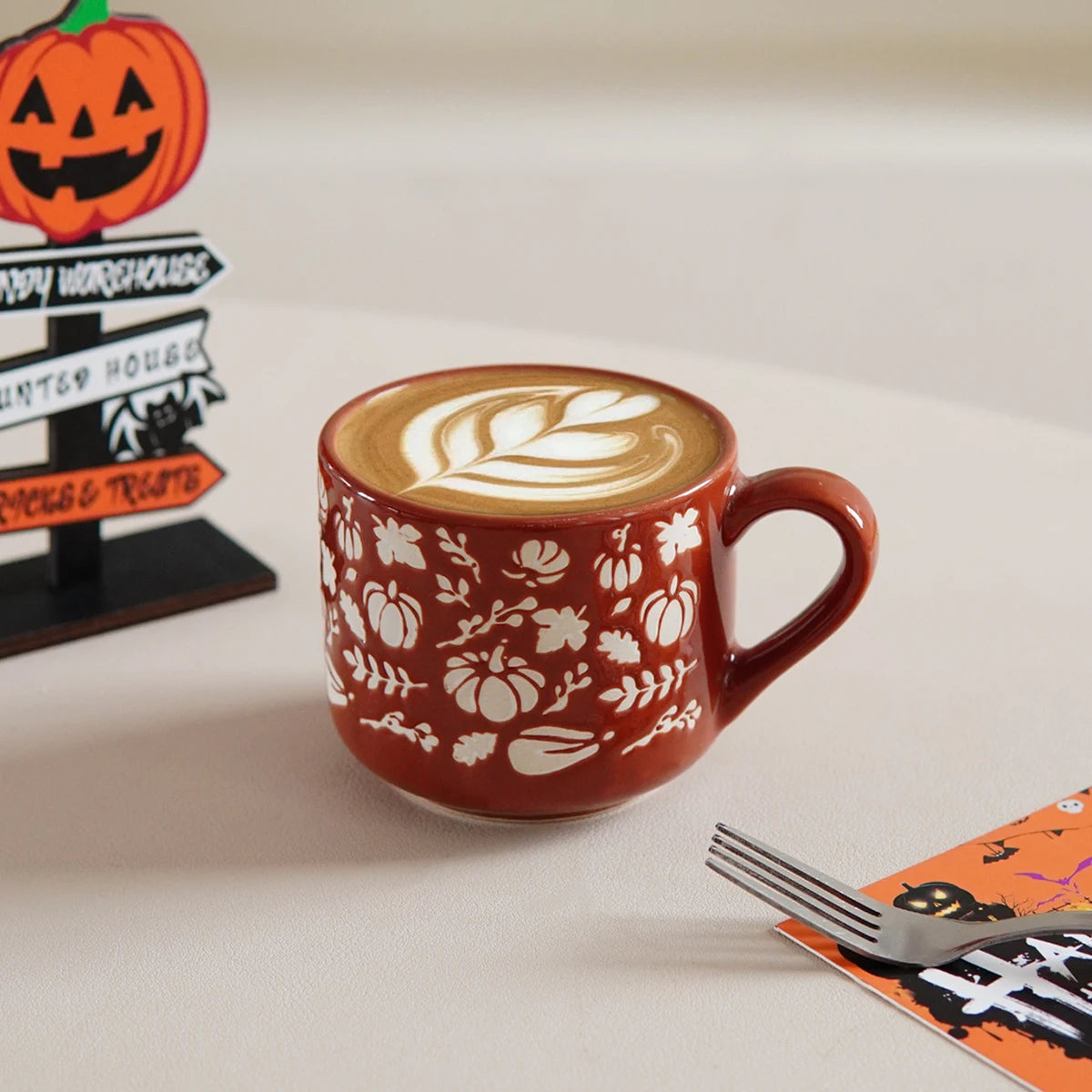 Red mug with white patterns on a white surface, featuring a latte art design.
