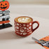 Red mug with white patterns on a white surface, featuring a latte art design.