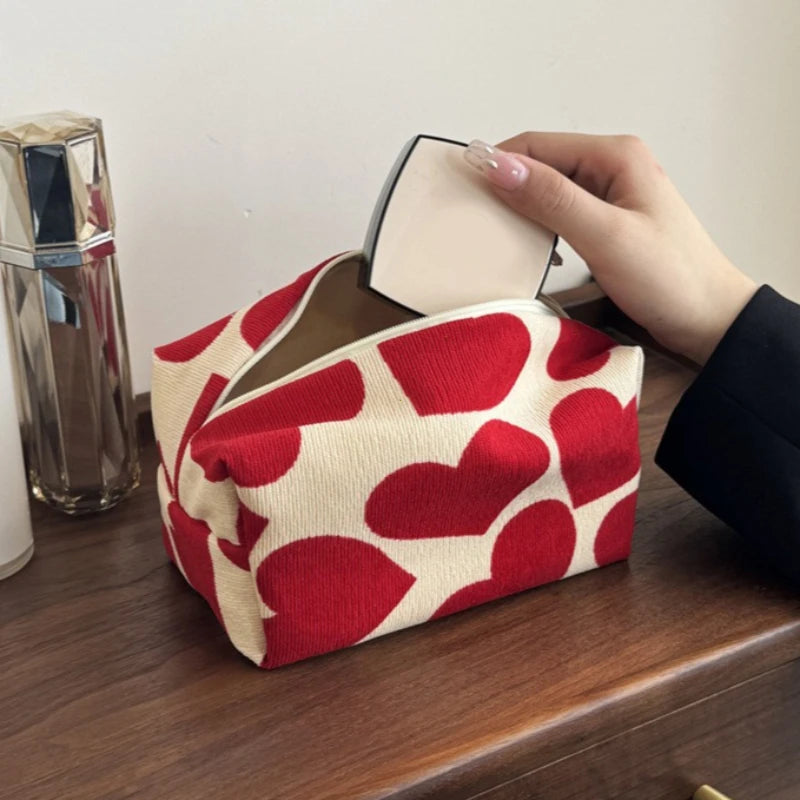 Red and white heart-patterned tissue box on a wooden surface with a hand taking out a tissue.