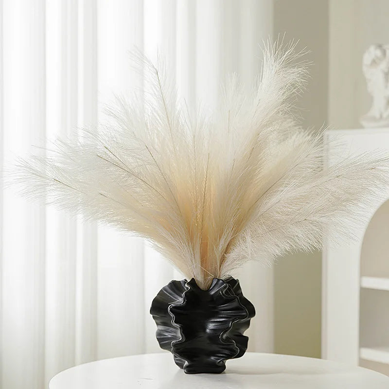 Black vase with dried pampas grass against a white curtain background
