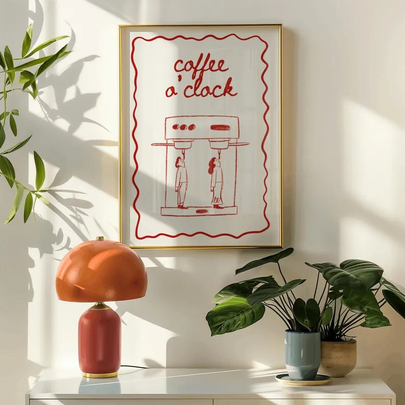 Framed artwork with 'coffee o'clock' text on a wall above a table with a lamp and plants.