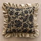 Decorative pillow with black floral pattern and beige ruffled edges on a beige background