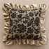 Decorative pillow with black floral pattern and beige ruffled edges on a beige background