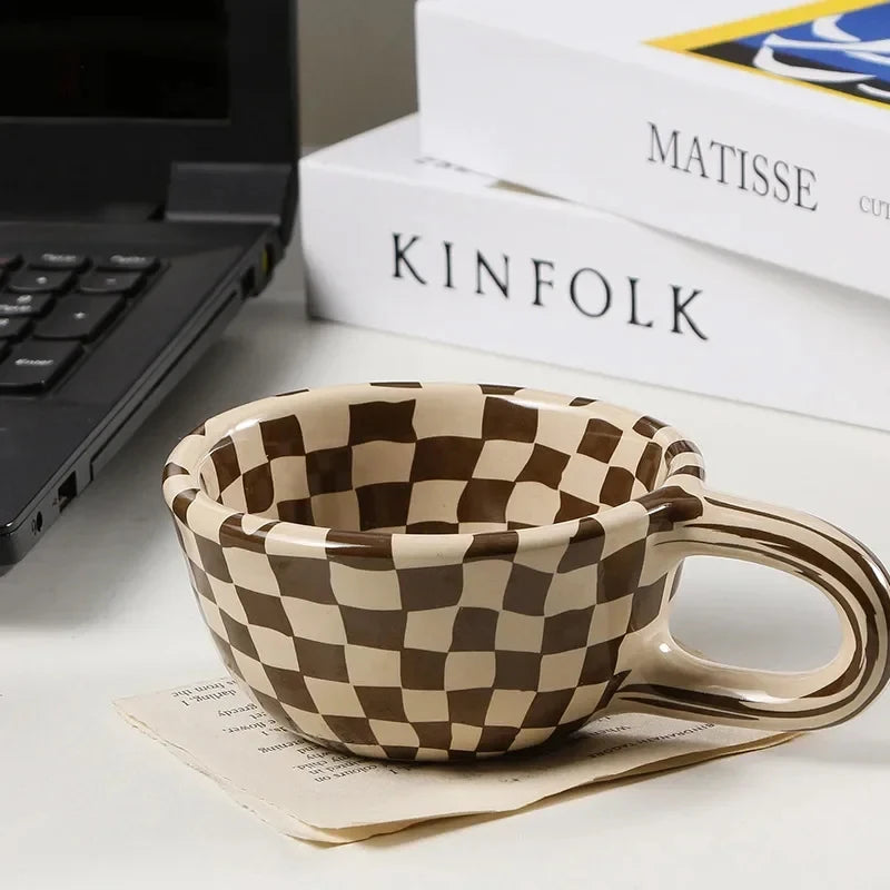 Checkered mug on a desk with books and a laptop in the background