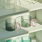 Green glass tumblers with pink handles on a white shelf
