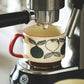 Espresso machine brewing coffee into a decorative mug with fruit design.