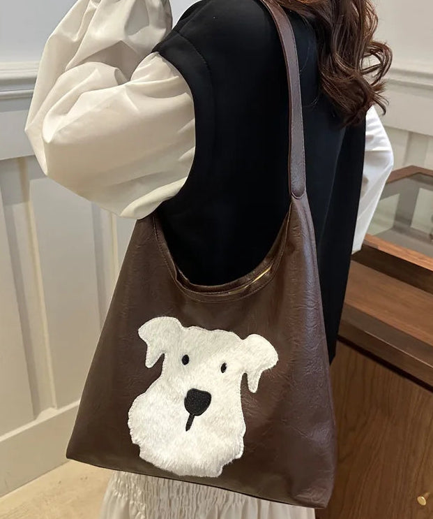 Brown tote bag with a white dog design held by a person indoors.