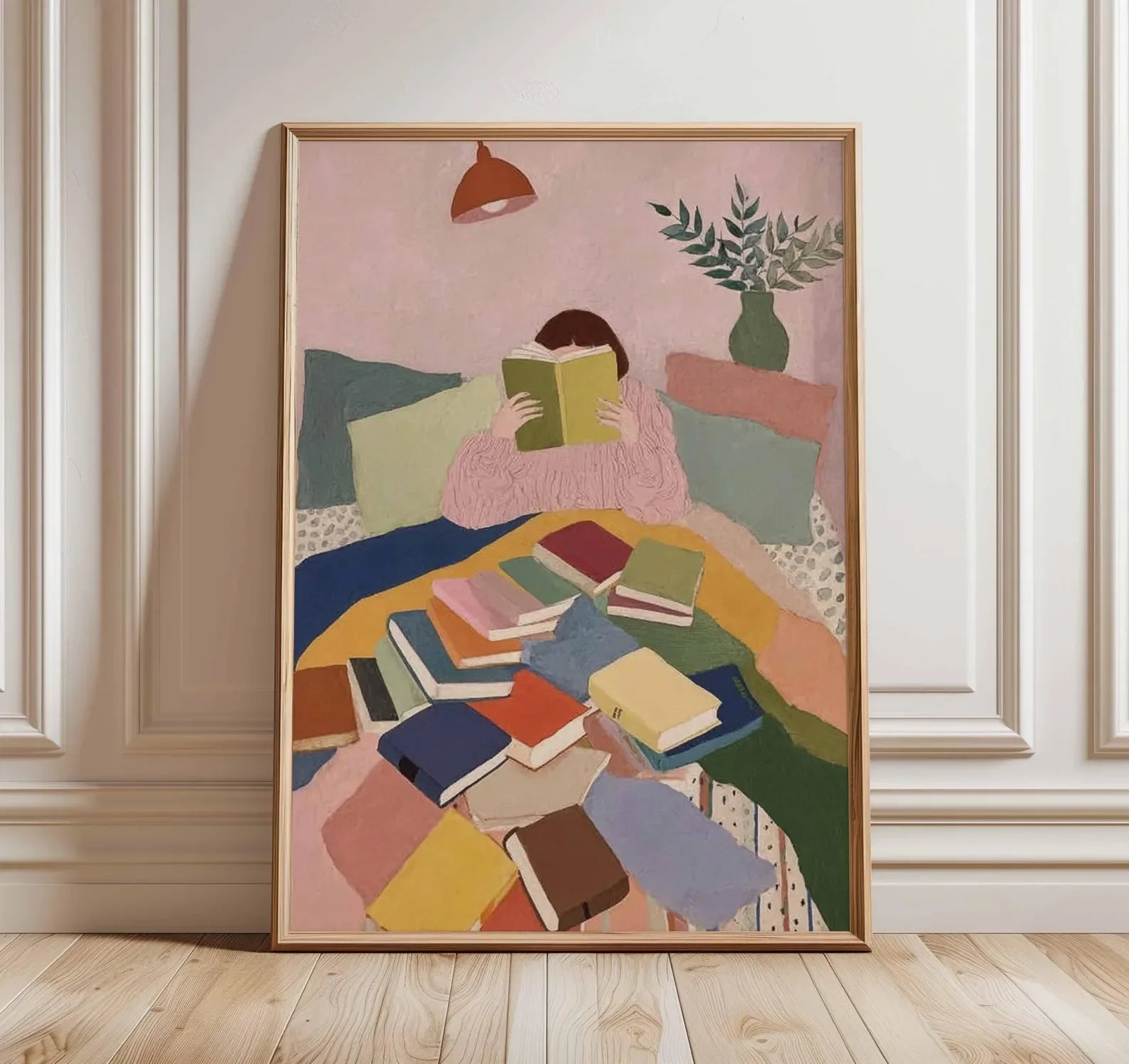 Framed artwork of a person reading a book on a colorful couch with books scattered around, in a room with a lamp and plant.