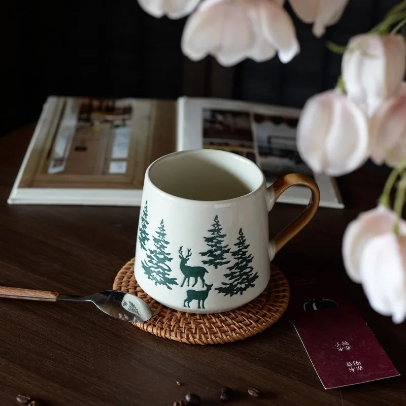 Mug with deer and tree design on a wooden table with flowers and books in the background