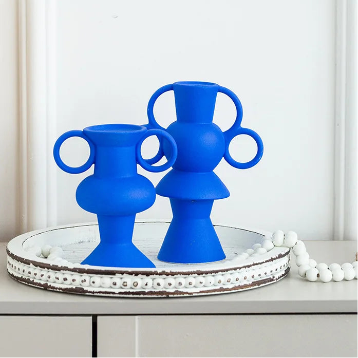 Two blue abstract vases on a decorative tray with a white wall and framed art in the background.